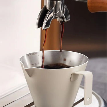Espresso being poured into a stainless steel portafilter on a white background